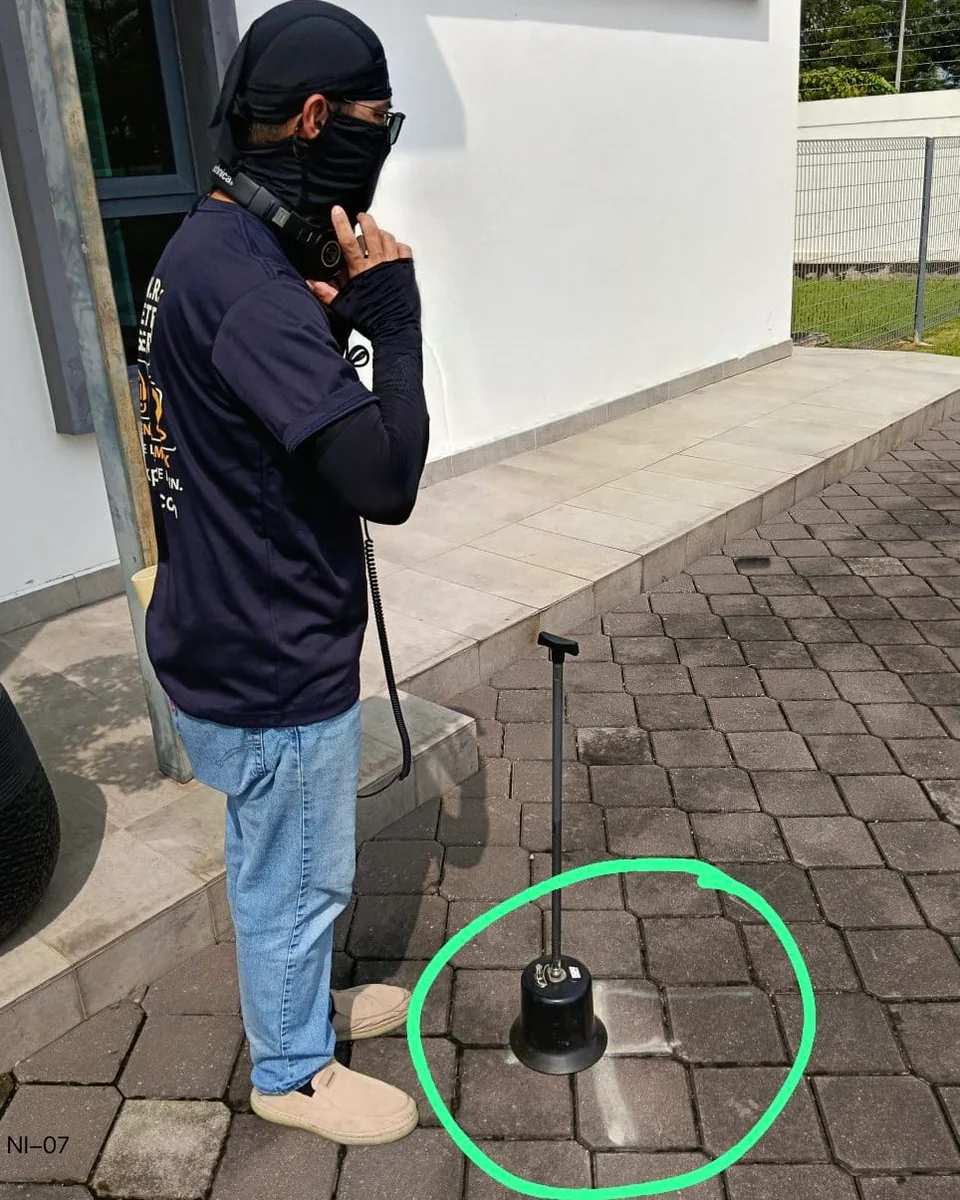 Juruteknik LeakPinpoint di sebelah peralatan mendengar tanah di kawasan berturap bertanda hijau.